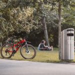 A red bicycle parked in a lush, sunny park with people relaxing nearby in Graz, Austria.